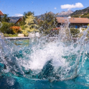 Wasserschwall mit spritzenden Tropfen über der türkisfarbenen Wasserfläche eines Timberra Naturpools.